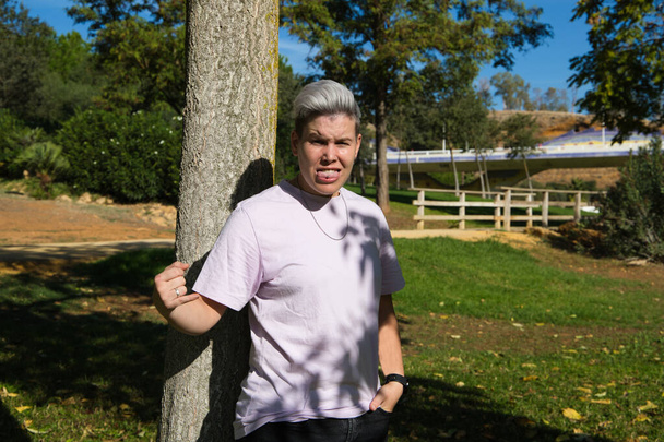 gender non-binary and androgynous person doing different postures and leaning on a tree. He is looking at the camera. Concept of non-binary and androgynous. Concept of diversity and expressions. - Foto, immagini