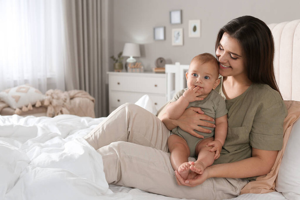 Happy young mother with her cute baby on bed at home - Photo, Image