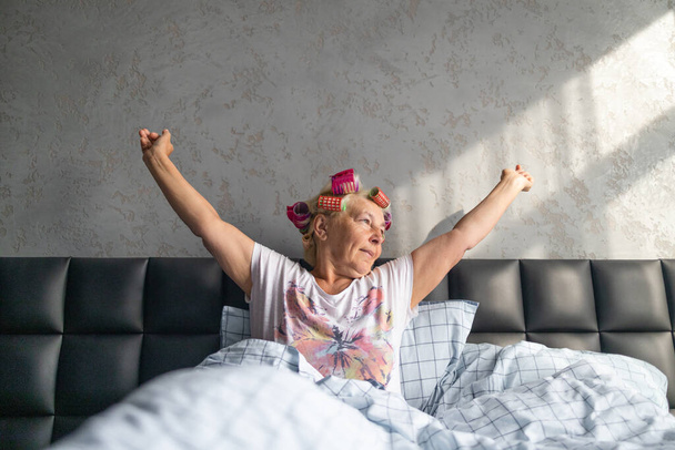 Orta yaşlı bir kadın sabahın erken saatlerinde yatak odasındaki beyaz battaniyeyle esniyor. Erken uyanma, uykusuzluk, aşırı uyku konsepti - Fotoğraf, Görsel
