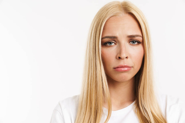 Young blonde woman in t-shirt frowning and looking at camera isolated over white background - Zdjęcie, obraz