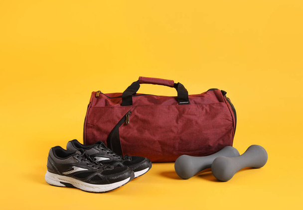 Sports bag and gym equipment on yellow background - Фото, зображення