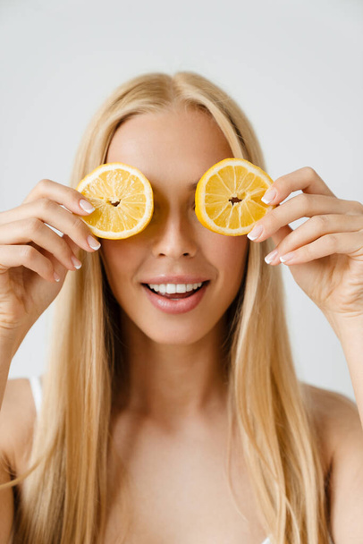 Молодая блондинка улыбается, позируя с кусочком лимона на белом фоне - Фото, изображение