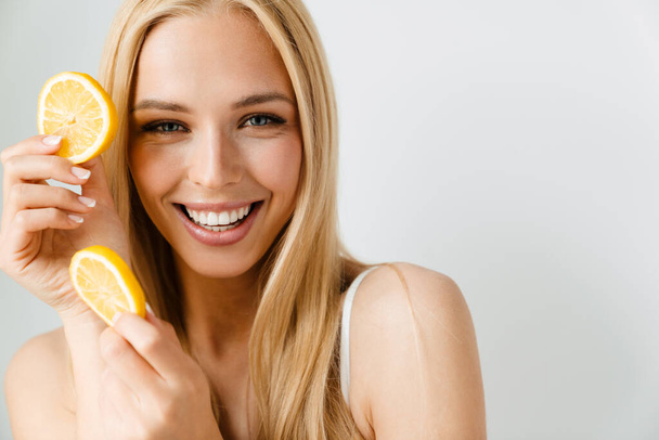 Молода блондинка посміхається, позує зі шматочком лимона ізольовано на білому тлі
 - Фото, зображення