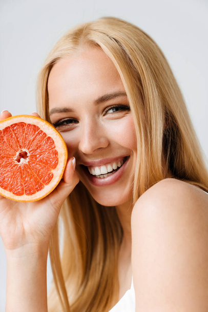 Young blonde woman smiling while posing with piece of grapefruit isolated over white background - Photo, image
