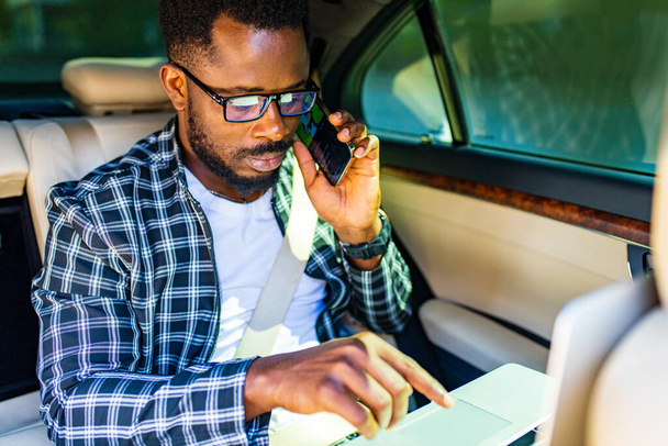 afrikkalainen amerikkalainen liikemies soittaa puhelun istuessaan auton istuimella - Valokuva, kuva