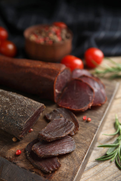 Delicious dry-cured beef basturma with rosemary and peppercorns on wooden table, closeup - Foto, Imagem