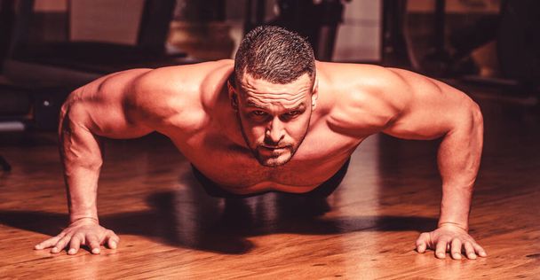 Muscular man doing push-ups on one hand against gym background. Sport. Muscular and strong guy exercising. Muscular male doing push-ups. Slim man doing some push ups a the gym. Man doing push-ups - Photo, Image