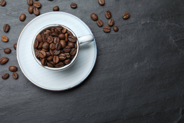 Cup with roasted coffee beans on black table, flat lay. Space for text - Photo, image