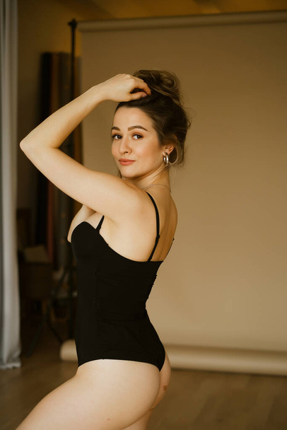 young beautiful caucasian woman in a black swimsuit with makeup and hairstyle, slender beautiful european lady a sexy image, stylish brunette with in a photo studio - Fotografie, Obrázek