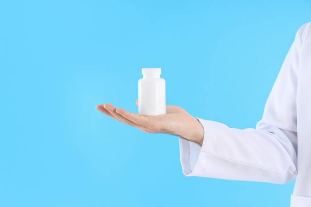 Male doctor holds bottle of pills on blue background - 写真・画像