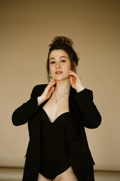 portrait of young beautiful caucasian woman in a black jacket , slender beautiful lady with hairstyle and makeup in a sexy image, stylish serious brunette in a business suit on beige background. - Zdjęcie, obraz