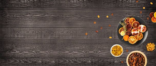 Αποξηραμένες φέτες πορτοκαλιού, σταφίδας και πορτοκαλιού αίματος σε φόντο ξύλου. Στεγνό σταφύλι, λεμόνι, μανταρίνι και sicilian πορτοκαλί mockup σε ξύλινο γραφείο φόντο πάνω όψη με αντίγραφο χώρου - Φωτογραφία, εικόνα