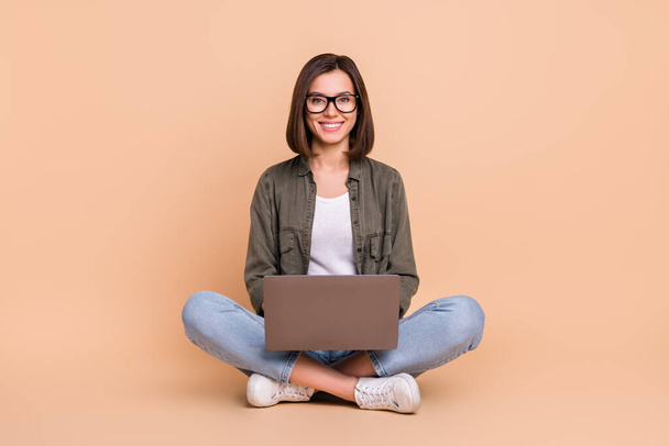 Photo of nice confident smart lady sit floor hold laptop wear glasses khaki shirt jeans isolated beige color background - 写真・画像