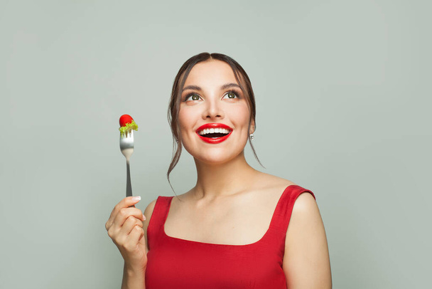 Szczęśliwa kobieta trzyma widelec z pomidorami i zieloną sałatą na białym tle. Koncepcja diety - Zdjęcie, obraz