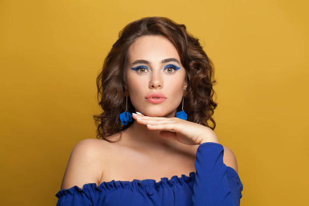 Lady in blue. Woman with brown curly hairstyle and makeup on yellow background - Fotó, kép