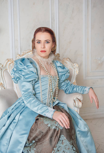 Beautiful young woman in medieval style blue dress sitting in the armchair - Foto, Imagen