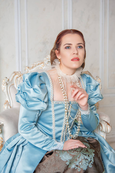 Beautiful young woman in medieval style blue dress sitting in the armchai - Photo, Image