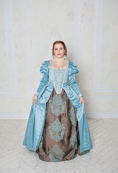 Ortaçağ tarzı mavi elbiseli güzel genç kadın odada duruyor. - Fotoğraf, Görsel
