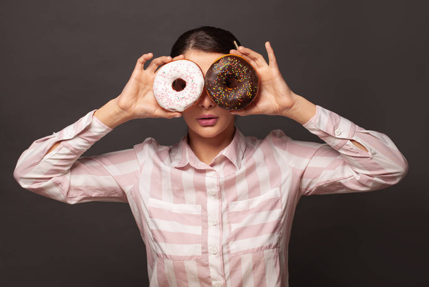 Cute woman covering her eyes with sweet donuts on black background. Diet concept - Fotoğraf, Görsel