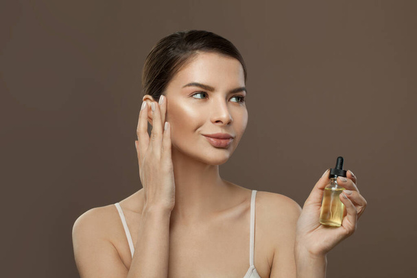 Lächelnde Frau mit Kosmetiköl in der Hand. Gesichtsbehandlung, Körperpflege, Wellness und alternatives Heilkonzept - Foto, Bild