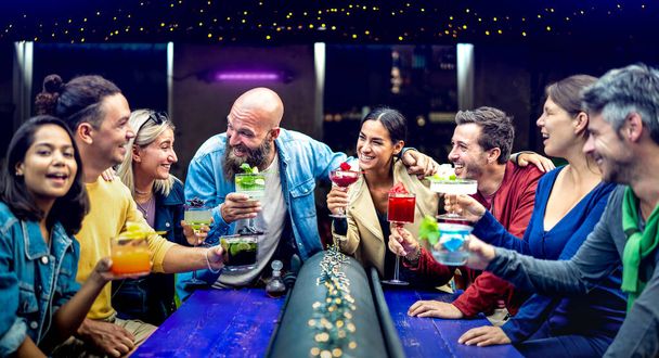 Wielokulturowi ludzie wznoszący toast za wielobarwne, fantazyjne drinki w barze mody - młodzi przyjaciele bawiący się razem pijący koktajl o happy hour - koncepcja czasu przyjęcia z jedzeniem i napojami na żywym filtrze indaco - Zdjęcie, obraz