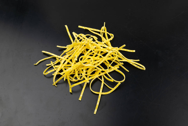 Яскраво-жовтий італійський tagliatelle pasta. Яйце саморобна суха локшина, тонкі стрічки макаронів, короткі неприготовані спагеті на чорному тлі. - Фото, зображення