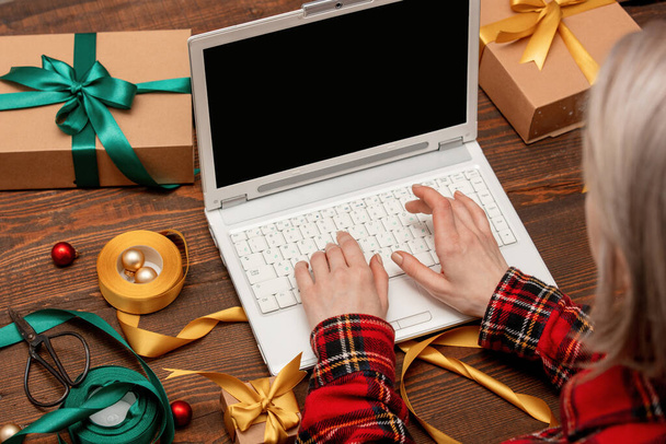 Frau arbeitet mit Laptop-Computer und wickelt Geschenkboxen auf einen Tisch. - Foto, Bild