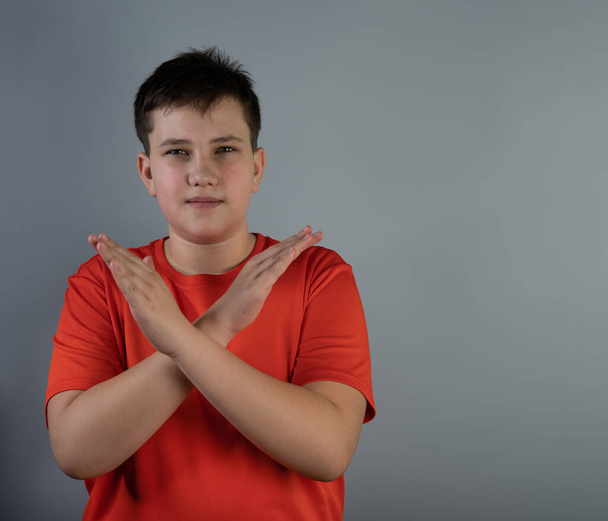 Серйозний хлопець, молодий чоловік у червоній футболці, дивиться в камеру зі схрещеними руками, показує знак зупинки. Підліток схрестив руки без знаку
 - Фото, зображення