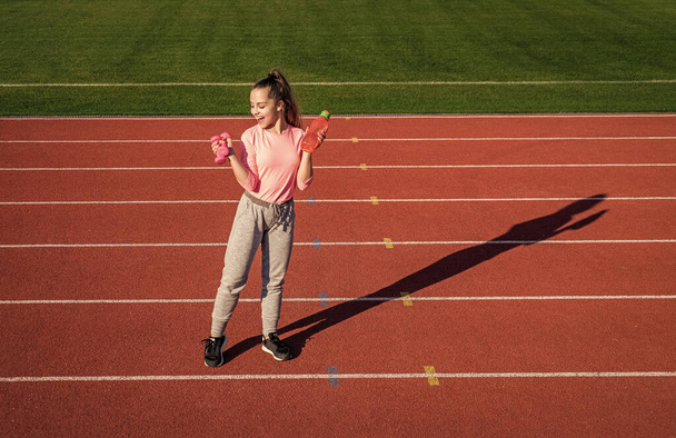 teen girl training with dumbbells and water bottle on outdoor stadium, fitness - Foto, Bild