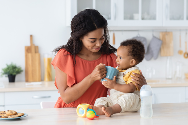 Junge schwarze Mutter trinkt aus ihrer Tasse ein Baby - Foto, Bild