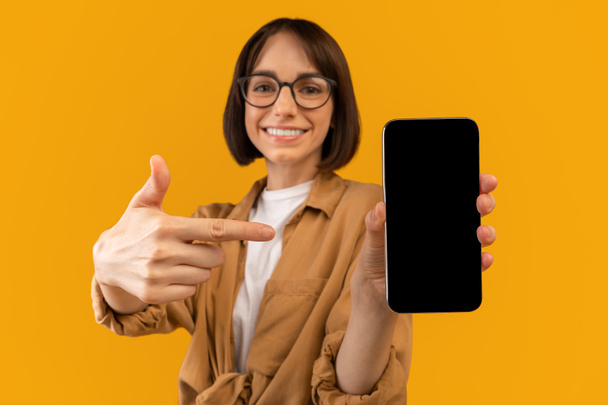 Gran aplicación. Mujer emocionada apuntando a la pantalla en blanco del teléfono inteligente, demostrando espacio libre para la aplicación móvil o el diseño del sitio web - Foto, Imagen