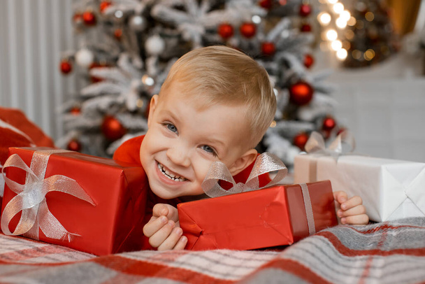 Happy boy laying on sofa with christmas gifts in decorated room - 写真・画像