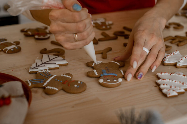 Christmas gingerbread painting. The girl icing the pattern on the cookie in the form of a ginger man. Homemade pastries. Preparing for the holiday. - Foto, Imagem