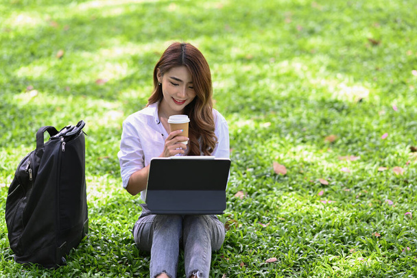 Kaunis aasialainen nainen juo kahvia ja työskentelee tietokone tabletti puistossa. - Valokuva, kuva