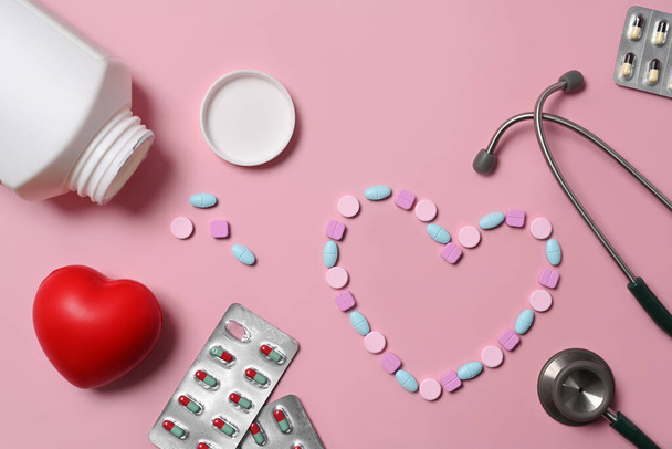 Medizintabletten, rotes Herz und Stethoskop auf rosa Hintergrund. Krankenversicherungskonzept. - Foto, Bild