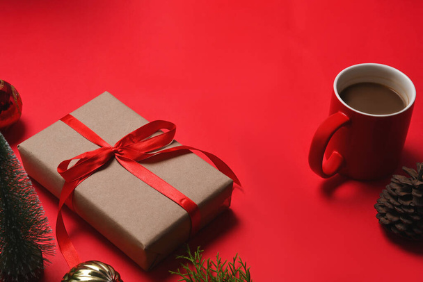 Christmas presents with red ribbon, pine cone, notebook and cup of coffee on red background. - 写真・画像