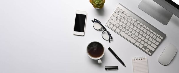 Escritorio de oficina blanco con taza de café, teléfono inteligente y computadora. - Foto, imagen