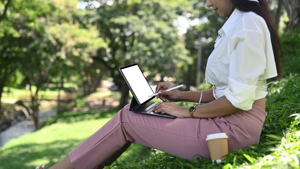 Junge Frau sitzt im öffentlichen Park und arbeitet mit Computer-Tablet. - Foto, Bild