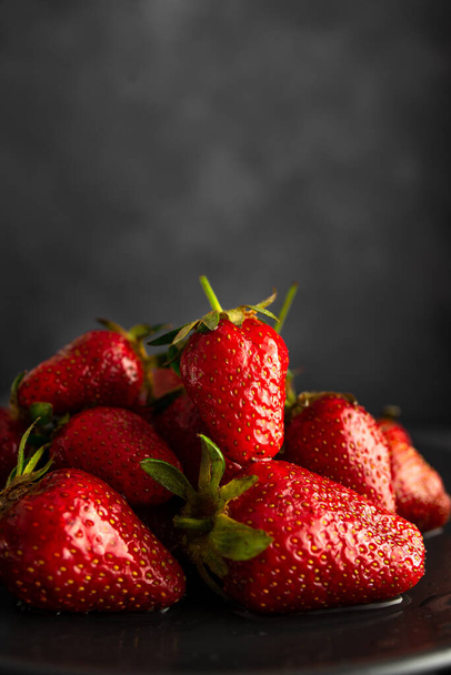 A vertical shot of a pile of fresh strawberries on a black plate - Fotografie, Obrázek