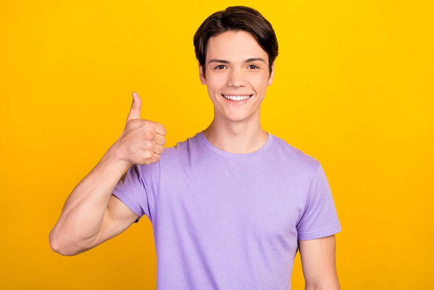 Portrait of attractive cheerful guy showing thumbup ad solution trust isolated over bright yellow color background - Zdjęcie, obraz