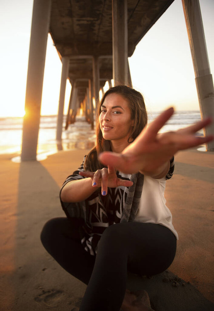 A young beautiful woman from the US reaching for the camera on the sandy beach at golden sunset - Foto, immagini