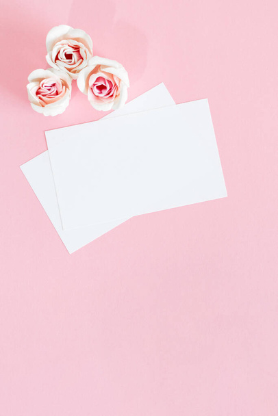 A top view of blank white greeting cards with pink rose flowers on a pink surface mock up. - 写真・画像