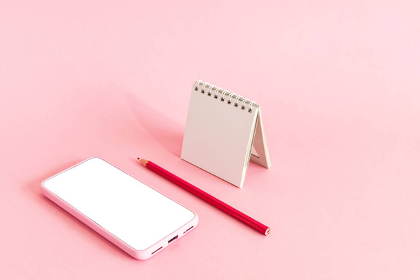 A smartphone with a blank screen, a calendar, and a pencil on a pink surface - online scheduled agenda - Photo, image