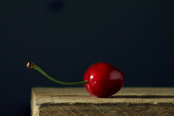 A selective focus shot of a cherry on a wooden surface with dark background - Fotoğraf, Görsel