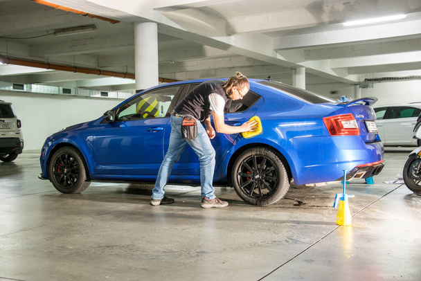 Брно, Чехія - 17 листопада 2021 року: в гаражі чоловік чистить блакитний спортивний автомобіль. Він полірує її жовтим прибиральником.. - Фото, зображення