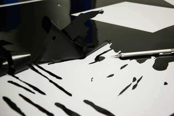 Деталь черной глянцевой фольги, вырезанной на плоттере и предназначенной для автомобильных наклеек - Фото, изображение