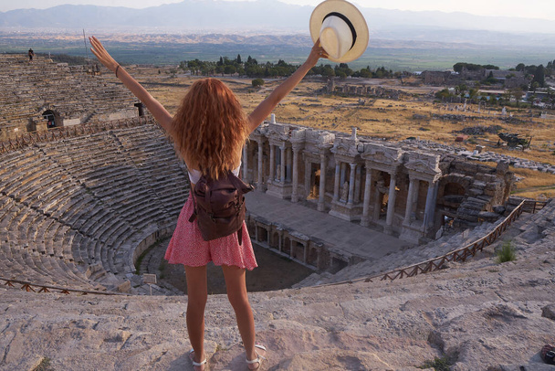 Hierapolis ancient city Pamukkale Turkey, young woman with hat watching sunset by the ruins Unesco. Traveler woman standing on theater Hierapolis ancient city in Pamukkale, Turkey                                - 写真・画像