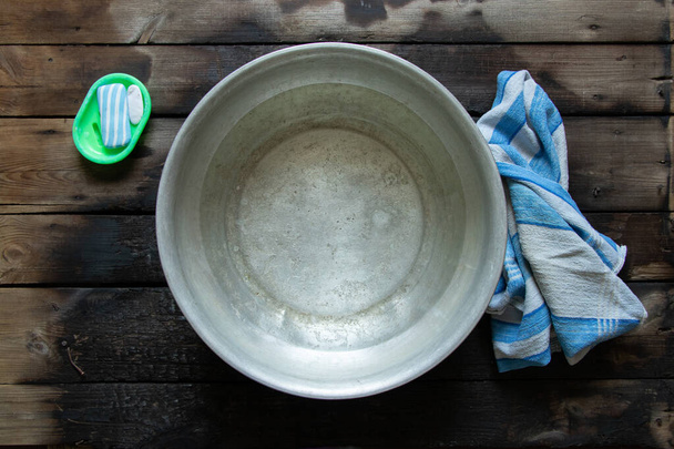 uma tigela de alumínio com água com sabão depois de lavar os pés está no chão ao lado de sabão e uma toalha, uma tigela de água no chão, lave em uma tigela - Foto, Imagem
