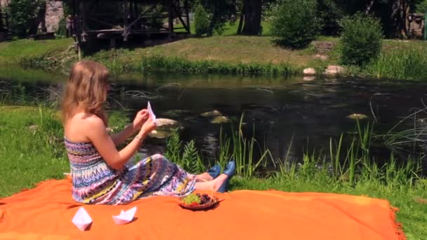 Tyttö tehdä paperi vene istua ruudullinen lähellä aaltoilu stream kesällä
 - Materiaali, video
