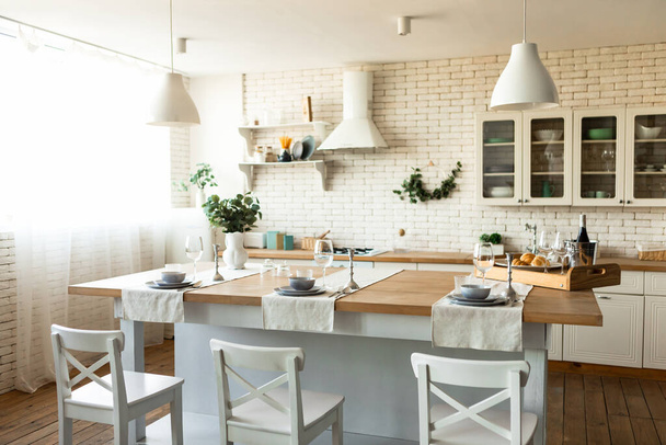 Útulná skandinávská kuchyně nebo jídelna interiér s dřevěným stolem a židlemi, lehký kuchyňský nábytek a nádobí - Fotografie, Obrázek